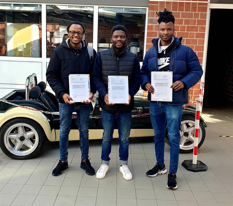 Three former ETALL students holding their official documents outside their company in Germany