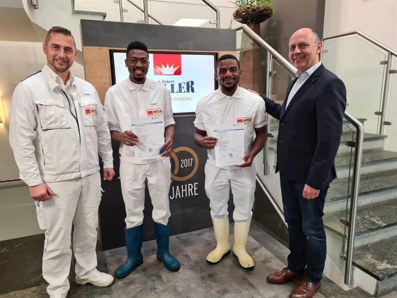 Two former ETALL students in work clothes, with their certificates and their German supervisors