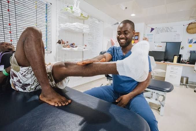 Ein lächelnder Physiotherapeut trainiert die Beweglichkeit des Beins eines Patienten